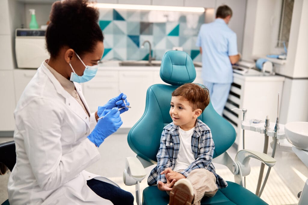 african american woman pediatric dentist in the bronx, talking to small boy on dentists chair